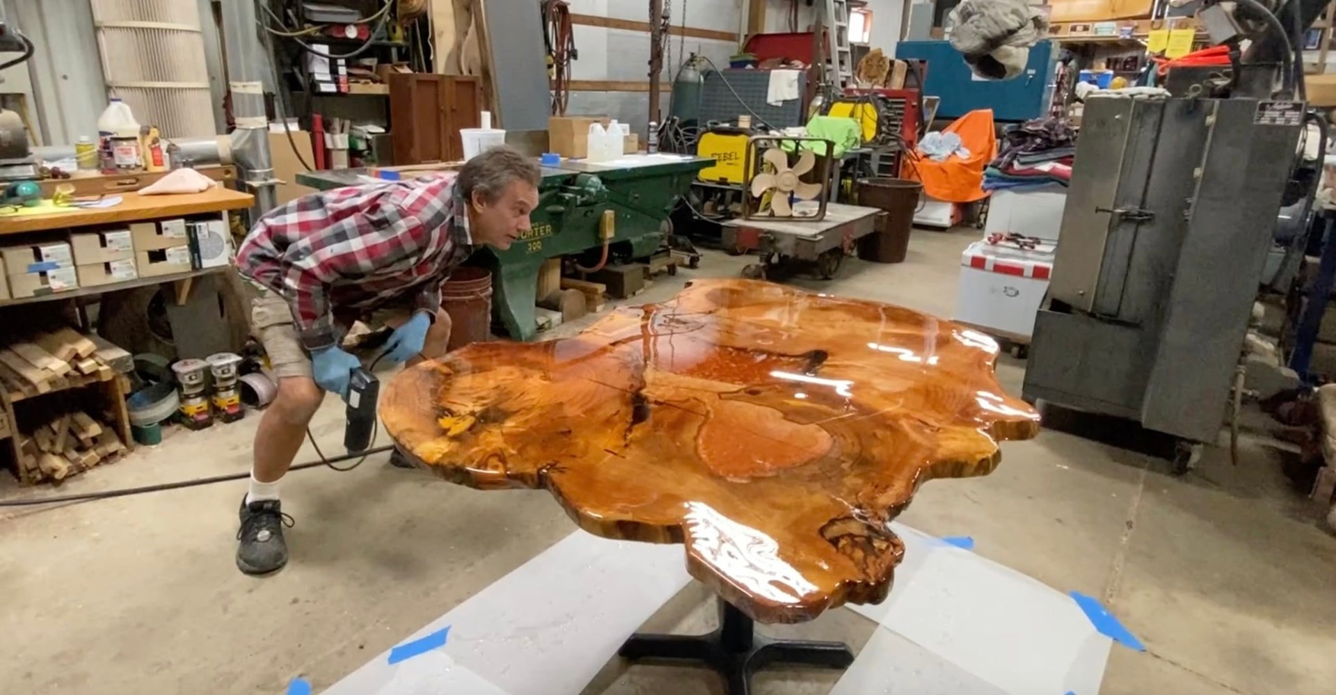 John Haling leaning low across a glossy freshly poured live-edge slab in his Whitmore Lake shop, checking the finish